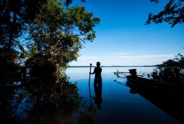 Silhouette of a man standing in a river surrounded by trees in the Amazon rainforest.