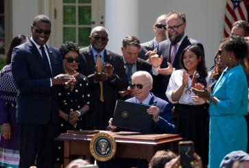 President Biden, surrounded by people, holds an executive order on environmental justice.