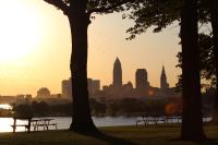 The Cleveland, Ohio skyline is seen between two trees and picnic tables.