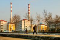A man walks down railroad tracks in front of apartment buildings with a coal plant in the distance.