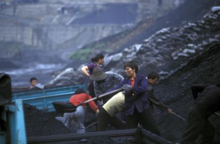 Workers shovel coal from large piles into carts in a village in China.
