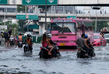 Motorcyclists, buses and pedestrians navigate a flooded, hectic city street.