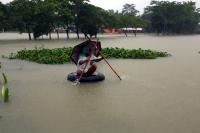 A man sits on a tire while wading with sticks through flood waters.