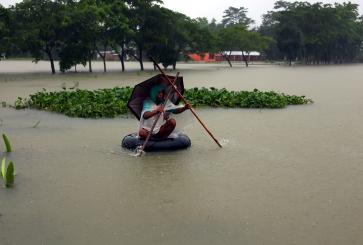 A man sits on a tire while wading with sticks through flood waters.