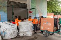 People handle large bags of recyclables outside a waste collection center.