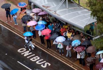 People wait under umbrellas at a bus stop in Brazil