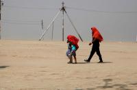 A family covers their heads with cloth for sun protection while walking near the Ganges river during a heatwave.