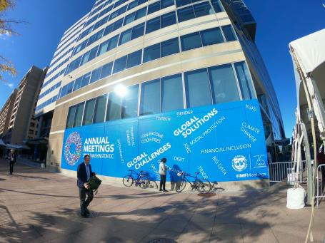 Buisness people walk past an office building with a large sign on it advertising an IMF meeting.
