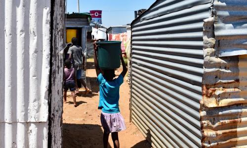 A young girl carries water through an informal settlement in Johannesburg, South Africa.