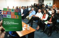 A pamphlet about Campinas's climate action plan is held up before a city hall audience.
