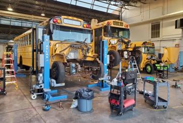 Two yellow school buses are hoisted above the ground to be converted to electric.
