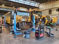 Two yellow school buses are hoisted above the ground to be converted to electric.