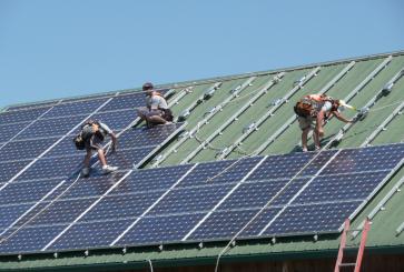 Three people work to install solar panels on the roof of a veterinary clinic.