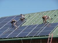 Three people work to install solar panels on the roof of a veterinary clinic.
