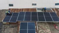 Two workers install solar panels on the corrugated metal roof of a shop.