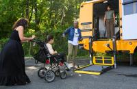 A girl in a wheelchair approaches the wheelchair lift on a school bus.