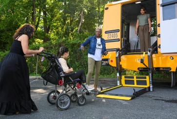 A girl in a wheelchair approaches the wheelchair lift on a school bus.