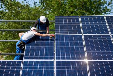 Two workers in hardhats install solar panels on a sunny day.