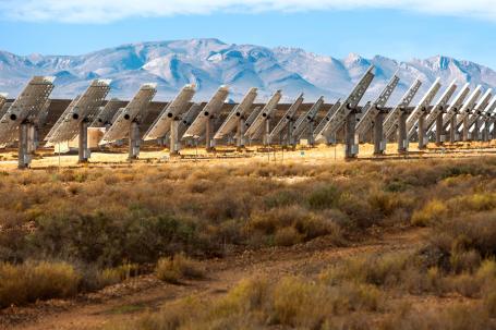 Rows of solar panels titled toward the sun with mountains in the background.