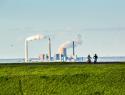 View of two mountain bikers on a grassy hillside with a coal plant in the distance.
