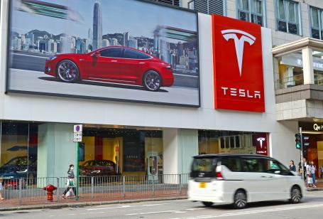 An advertisement for Tesla with a red car hangs on a wall above a street in Hong Kong.
