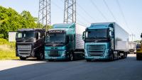 Three zero-emission trucks parked on the street with powerlines and trees.
